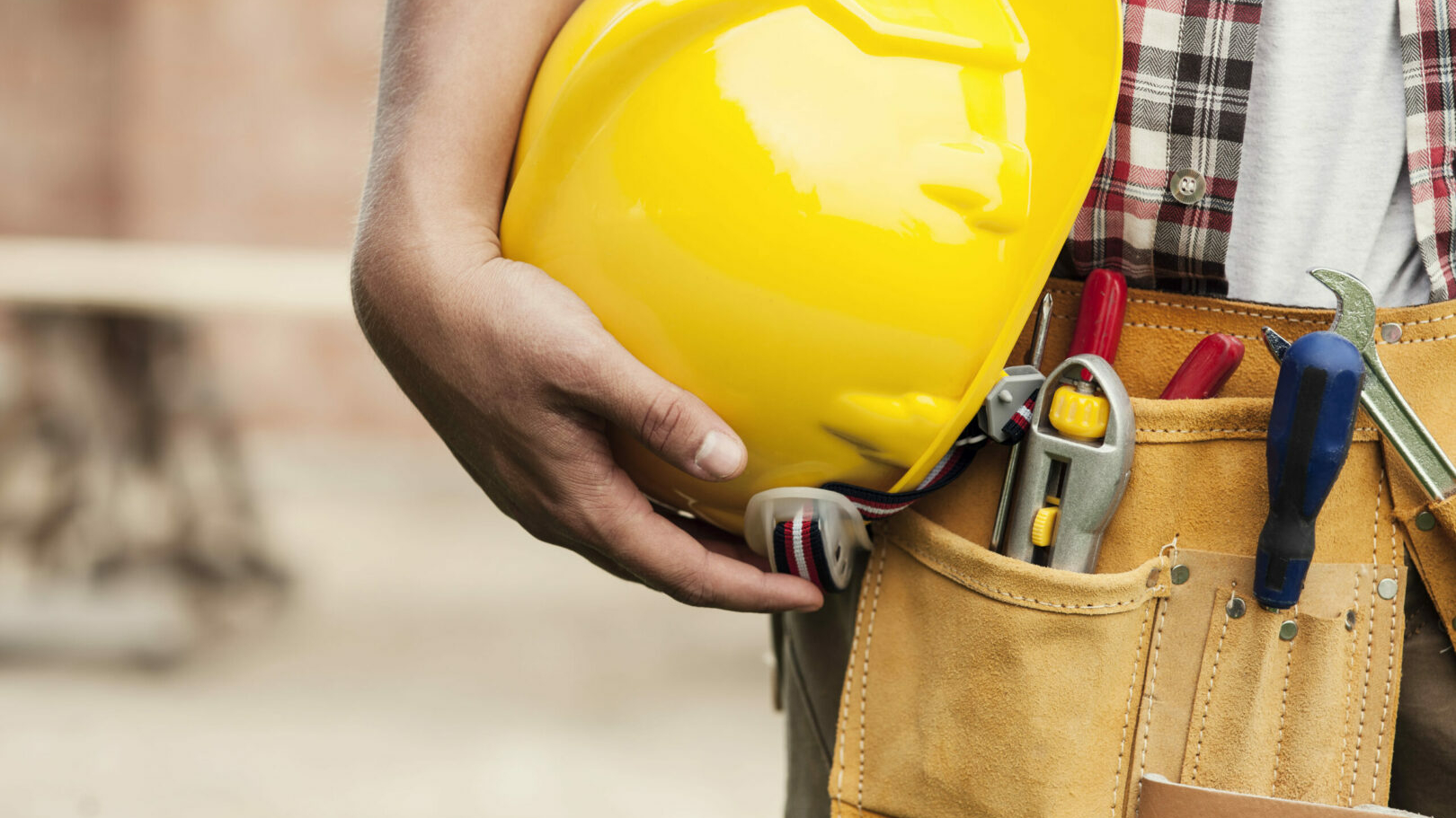 image de la taille d'une personne équipée d'une ceinture à outils. La personne tient un casque jaune dans ses mains contre sa taille.