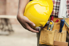image de la taille d'une personne équipée d'une ceinture à outils. La personne tient un casque jaune dans ses mains contre sa taille.