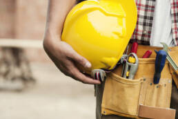 image de la taille d'une personne équipée d'une ceinture à outils. La personne tient un casque jaune dans ses mains contre sa taille.