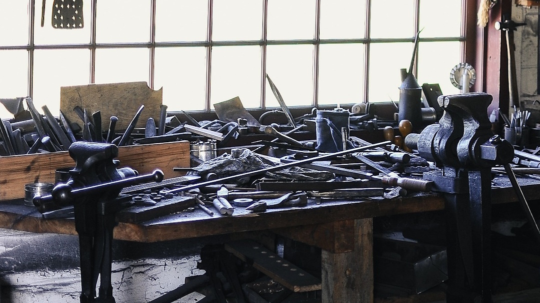 Photo d'un établi à l'intérieur d'un atelier. Cet établi est rempli d'outils en bazar devant une fenêtre à carreaux. Il n'y a pas de gestion de matériel à cet endroit.