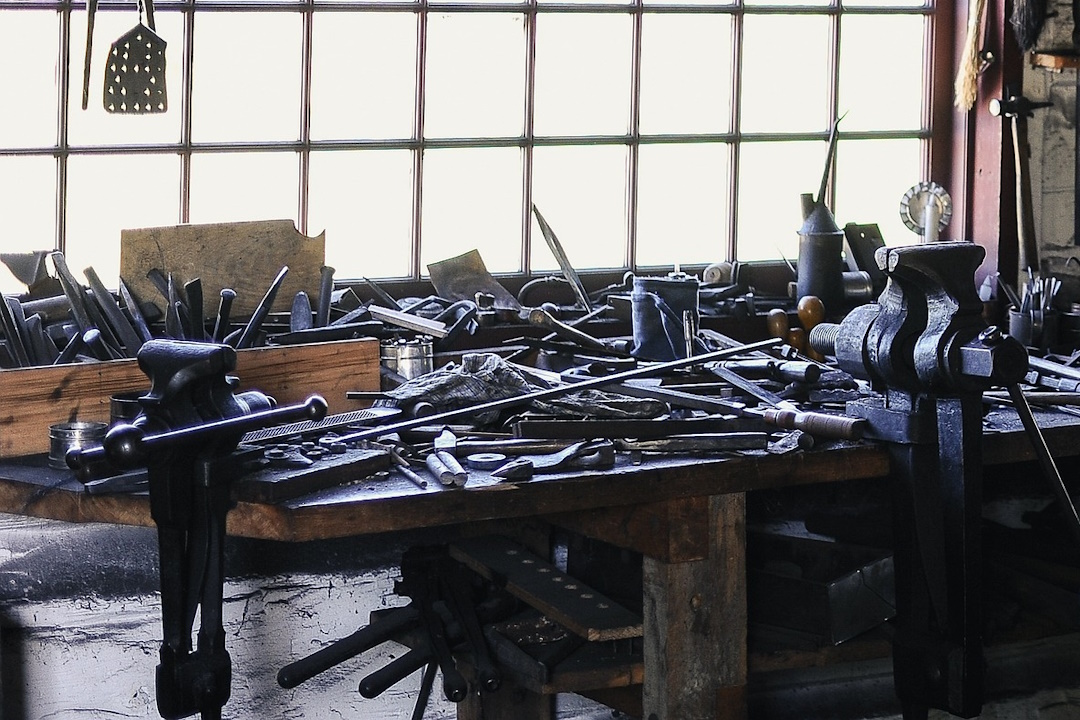 Photo d'un établi à l'intérieur d'un atelier. Cet établi est rempli d'outils en bazar devant une fenêtre à carreaux. Il n'y a pas de gestion de matériel à cet endroit.