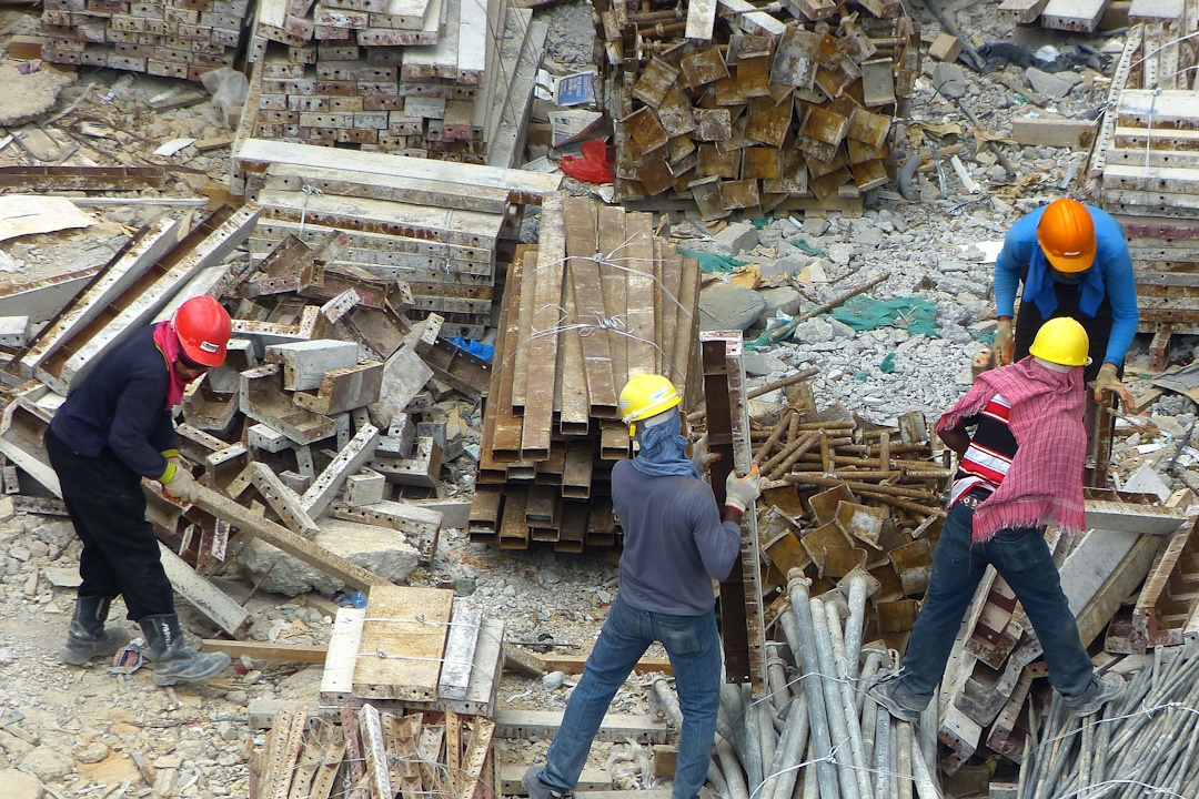 Cette photo prise en hauteur montre des ouvriers travaillant sur un chantier en contrebas. Ils sont au milieu de matériaux et de matériels pour faire leur travail.