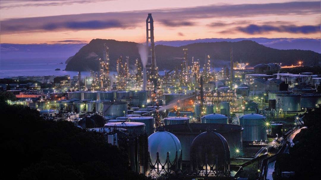 Photographie en hauteur d'une ville devant une production d'énergie au coucher de soleil. Image par Tasukaran.